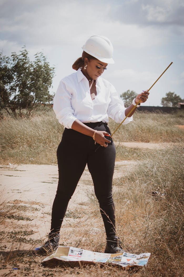 brand-03 African female civil engineer wearing hard hat measuring outdoors with a tape. Ideal for industry or construction themes.