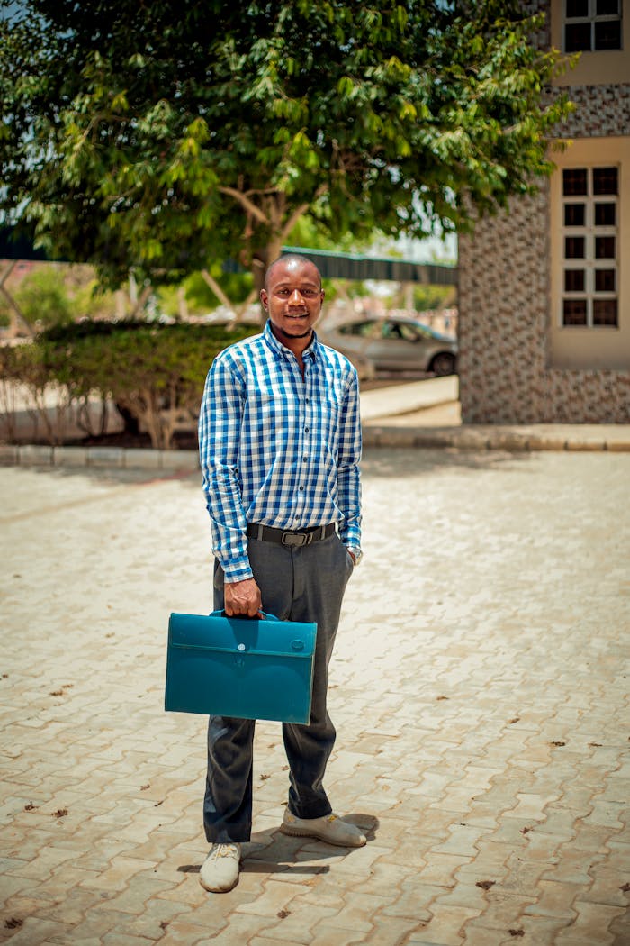 creative-03 Smiling businessman in checkered shirt holding a blue briefcase outdoors on a sunny day.
