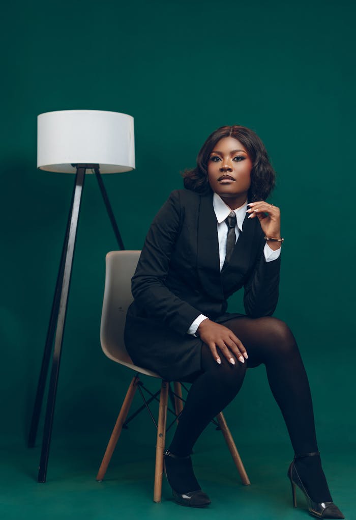 creative-02 Confident woman in business attire sitting beside a modern lamp.