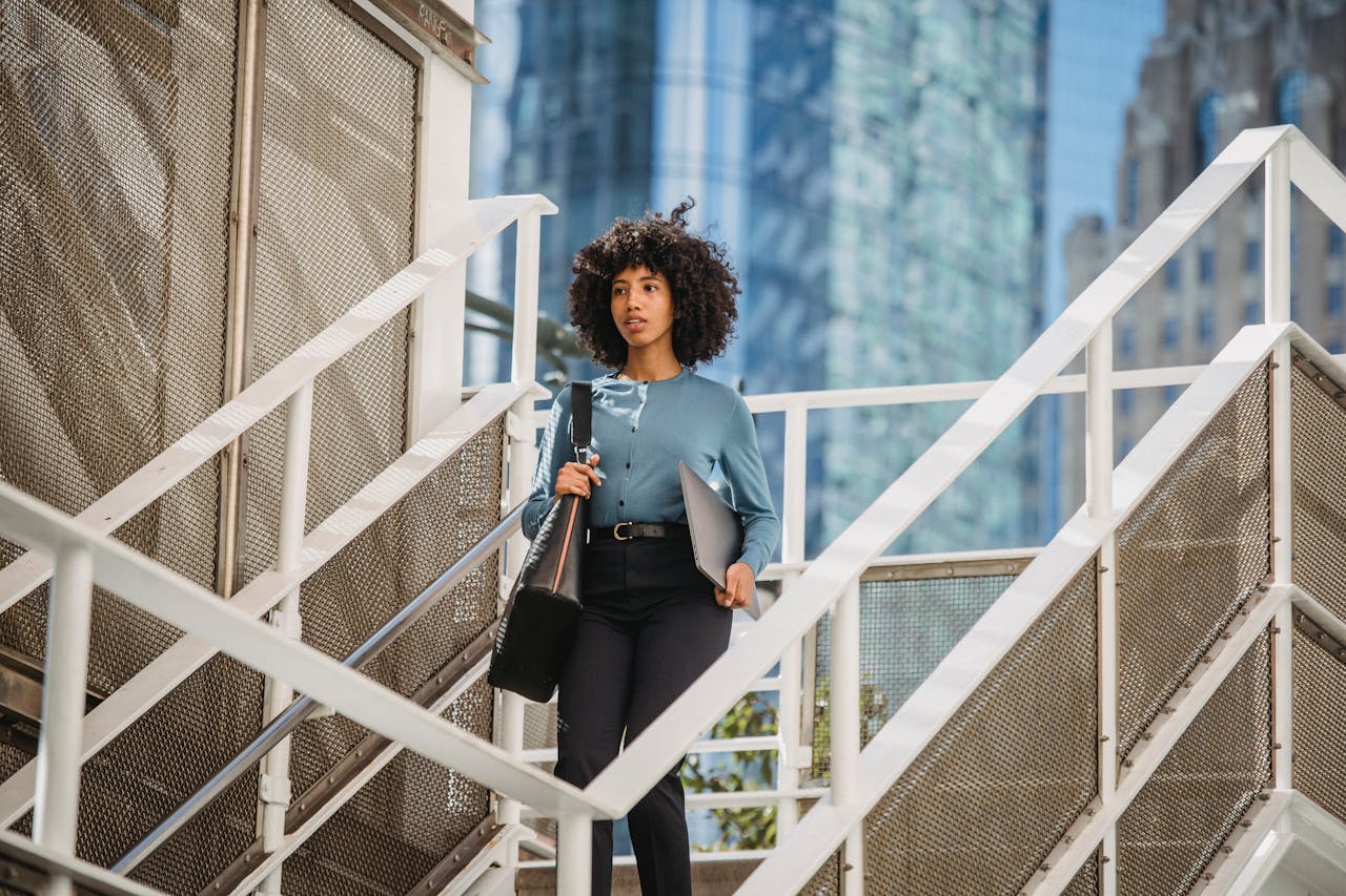 Confident woman carrying a laptop descends stairs in an urban business district.