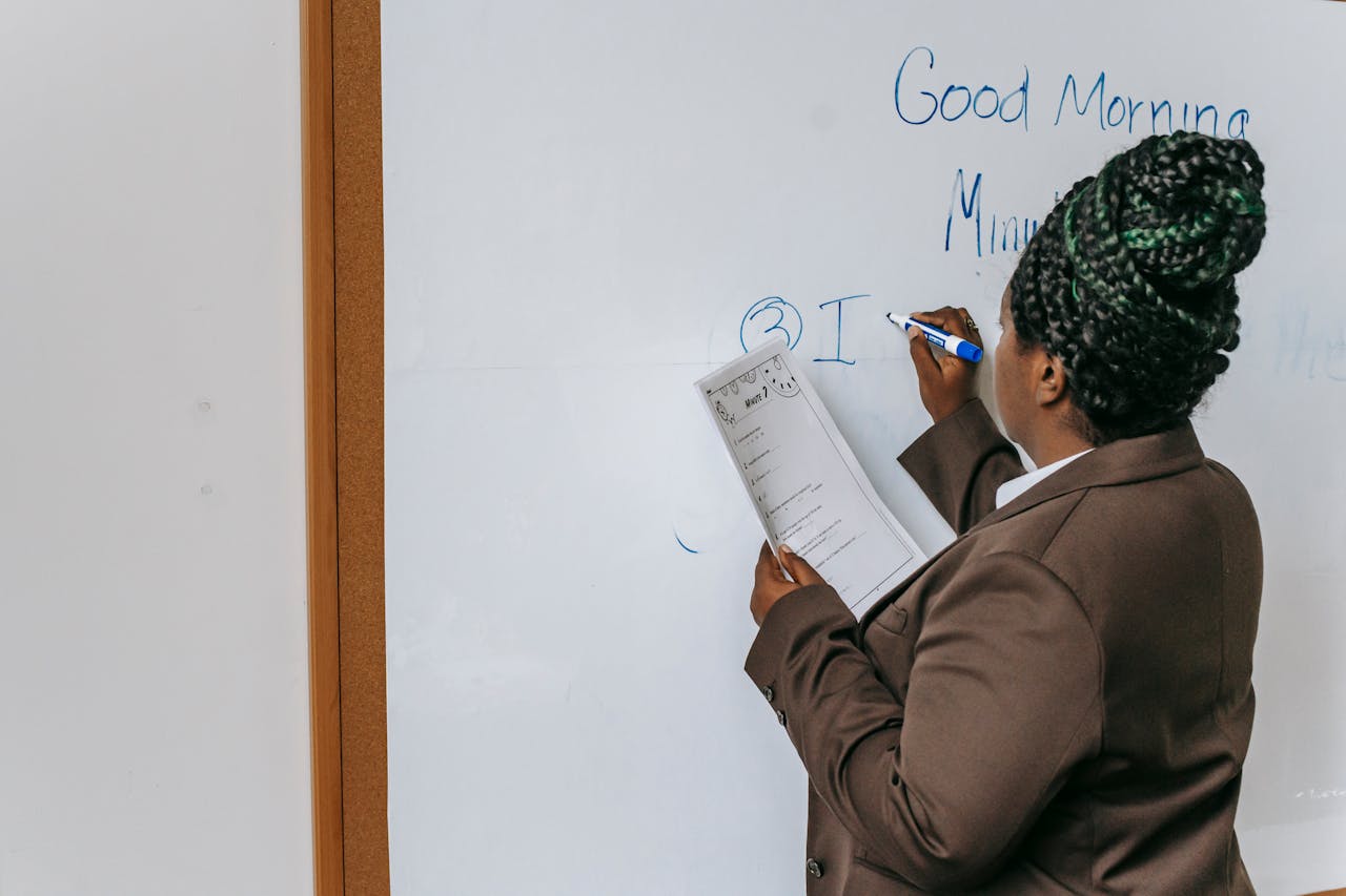 mobile-01 Back view anonymous African American female teacher wearing formal suit writing information on paper in auditorium