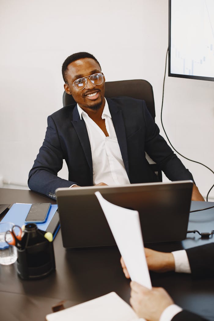digital-01 Smiling businessman in suit working with laptop in modern office setting, engaging in discussion.