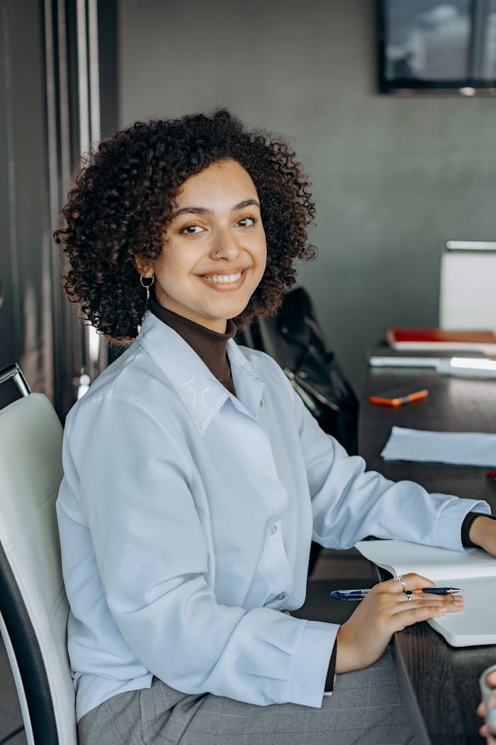 brand-02 Bright and confident woman smiling at her desk in a modern office environment.